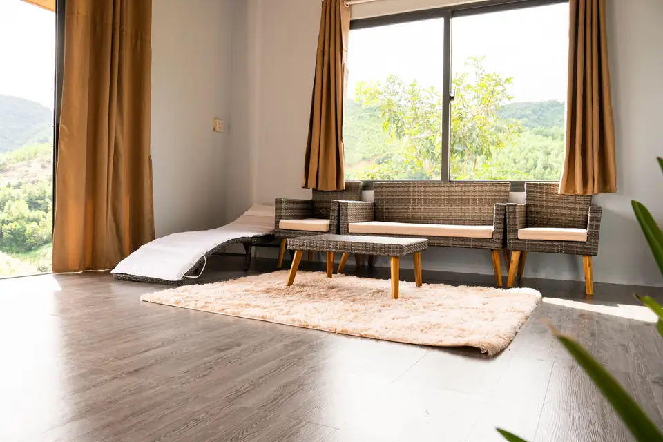 Phòng khách nhà mẫu: sàn gỗ, sofa, hai khung cửa kính lớn nhìn ra đồi
