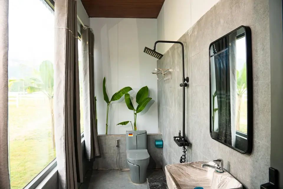 Phòng tắm nhà mẫu tường xi măng, gương lớn, cửa sổ nhìn ra cây xanh